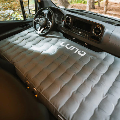 A grey LUNA inflatable mattress perfectly fits an RV rental van's front seats & dashboard, creating a cozy sleeping area for travelers.