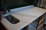 Compact RV rental kitchen: white counter with sink, modern faucet, and visible water on its gray-patterned surface.
