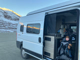 Winter RV rental trip: A happy baby in a carrier inside a Solis camper van, parked amidst snowy mountains.