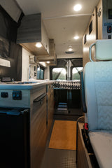 Step inside this modern RV rental: a compact interior features a kitchenette, bed, and ample lighting for comfortable living.