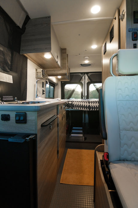 Step inside this modern RV rental: a compact interior features a kitchenette, bed, and ample lighting for comfortable living.