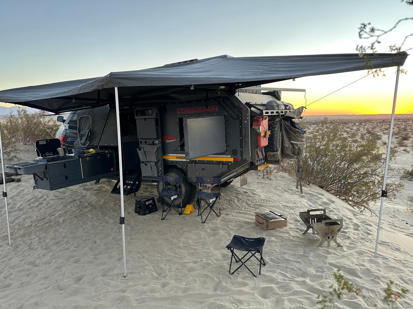 An off-road camper trailer, ideal for RV rental, with an awning & kitchen set up on sandy terrain at sunset. — photo 20