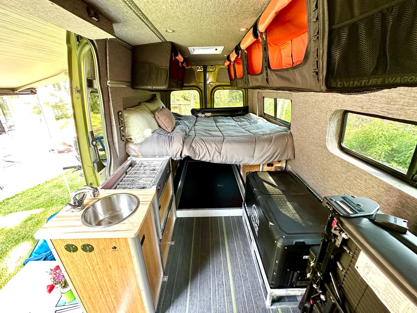 RV rental van interior features a cozy bed, kitchenette with sink/stove, and overhead storage for adventurers.