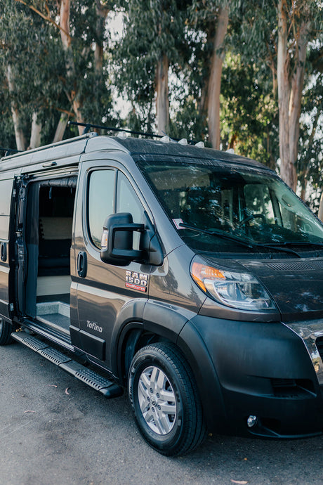 This dark gray Ram ProMaster campervan RV rental, branded 'Tofino,' with its side door open revealing the interior, awaits your adventure.