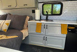 Stylish RV rental interior with a cozy bed, modern kitchenette featuring white subway tiles, and grey cabinets.