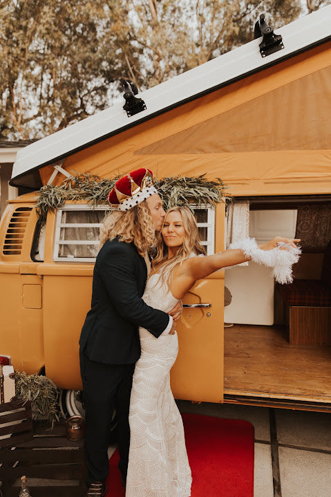 Happy couple by their vintage yellow VW camper rv rental! Crowned groom kisses the bride on a red carpet. — photo 8