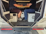 Two people sit face-to-face at a table inside an rv rental camper. The cozy interior features speakers and seating.