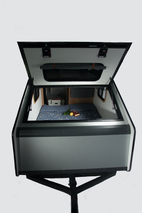 This open mini camper, ideal for RV rental, showcases a cozy bed with a starry blanket, a book, and storage. Ready for your adventure.