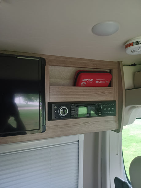 Inside an RV rental: View of the entertainment unit, showing a Jensen media console, TV, and a red first aid kit in a cubby.