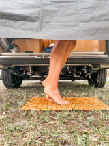 Enjoying a refreshing outdoor shower with an RV rental, feet on a wooden mat, surrounded by nature.