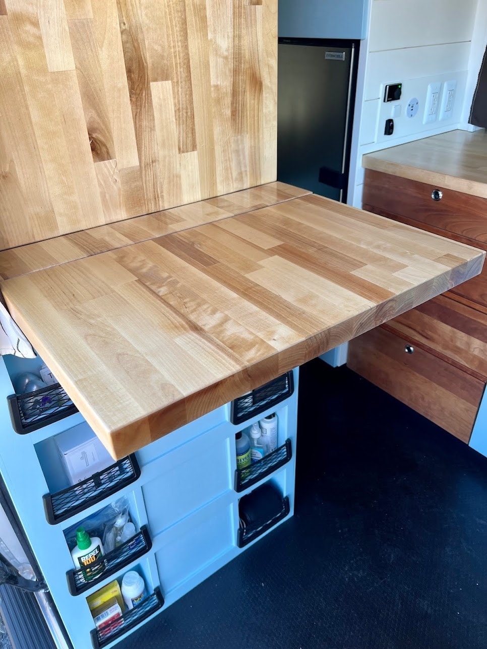 Efficient rv rental: light wood countertop/desk, light blue storage bins with supplies, and a mini-fridge. Smart van interior. — photo 8