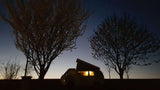 Cozy camper van glowing at dusk, framed by trees. Perfect RV rental for your next outdoor adventure!