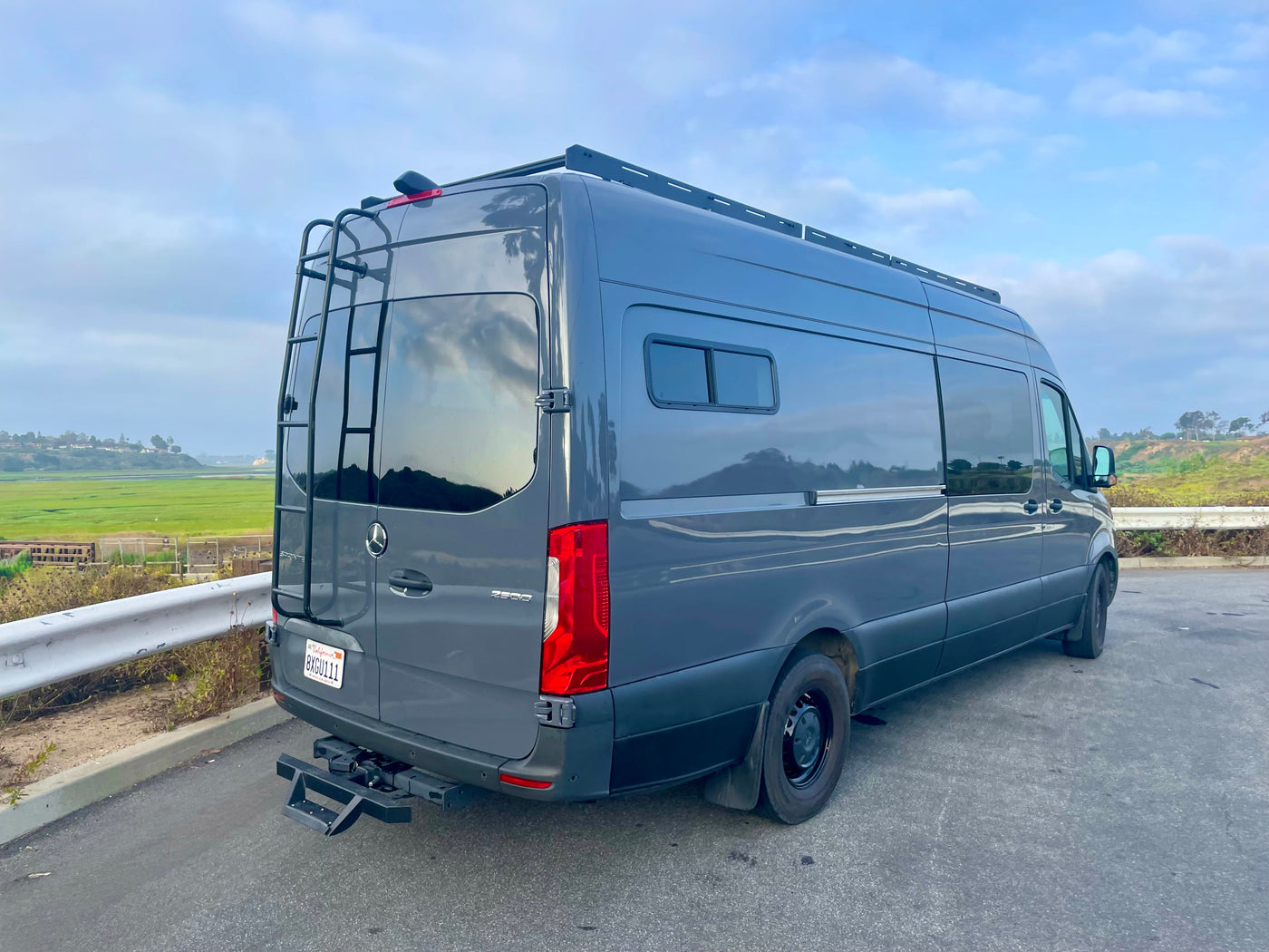 Sleek gray Sprinter camper van for rv rental, featuring a rear ladder and roof rack, overlooking wetlands. — photo 9