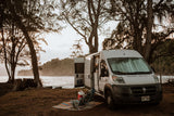 RV rental camper van camped by the ocean, with chairs and cooler set up for a relaxing beachside escape.