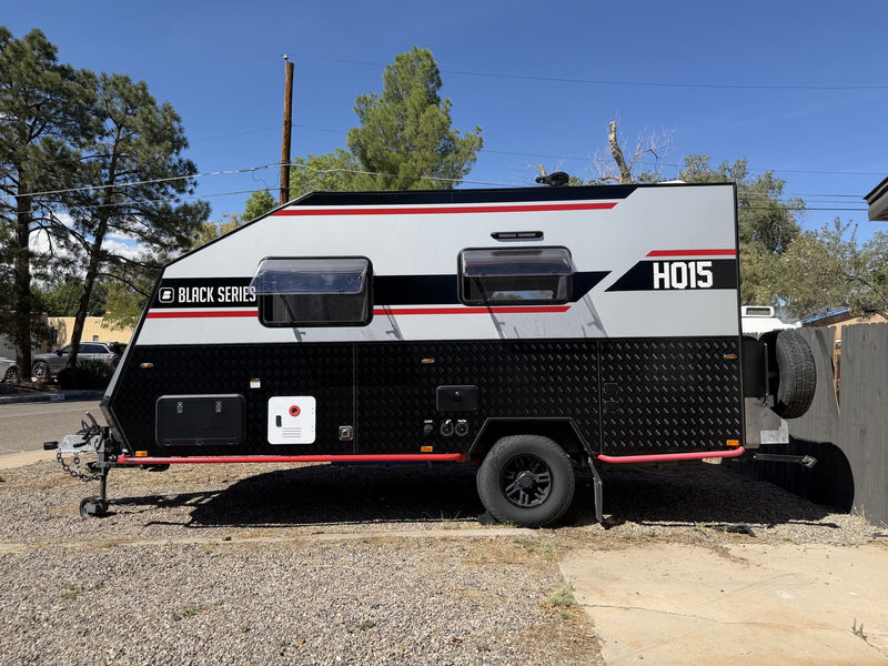 2022 Black Series HQ15 off-road trailer parked on gravel, full driver-side profile in bright sun showing the white and black body with red accent stripe, HQ15 graphics, checker-plate lower skin, single-axle black alloy wheel and red chassis rail — photo 1