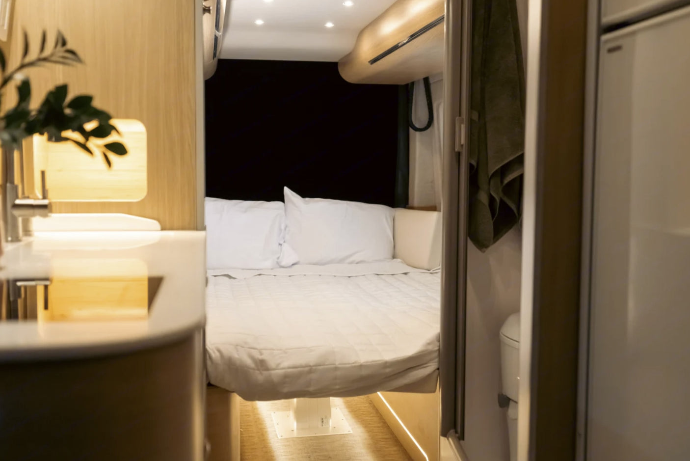 Inside a modern rv rental: A well-appointed sleeping area with white bedding, adjacent sink, and compact bathroom.