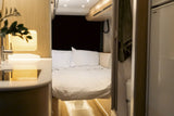 Inside a modern rv rental: A well-appointed sleeping area with white bedding, adjacent sink, and compact bathroom.