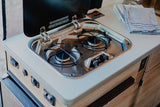 Compact Suburban 2-burner gas cooktop with a protective glass lid in this rv rental, ideal for cooking in your travel kitchen.