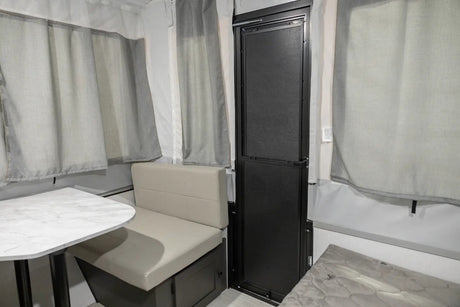 Cozy RV rental interior with a light dining booth, table, and a black entry door, surrounded by grey curtains.