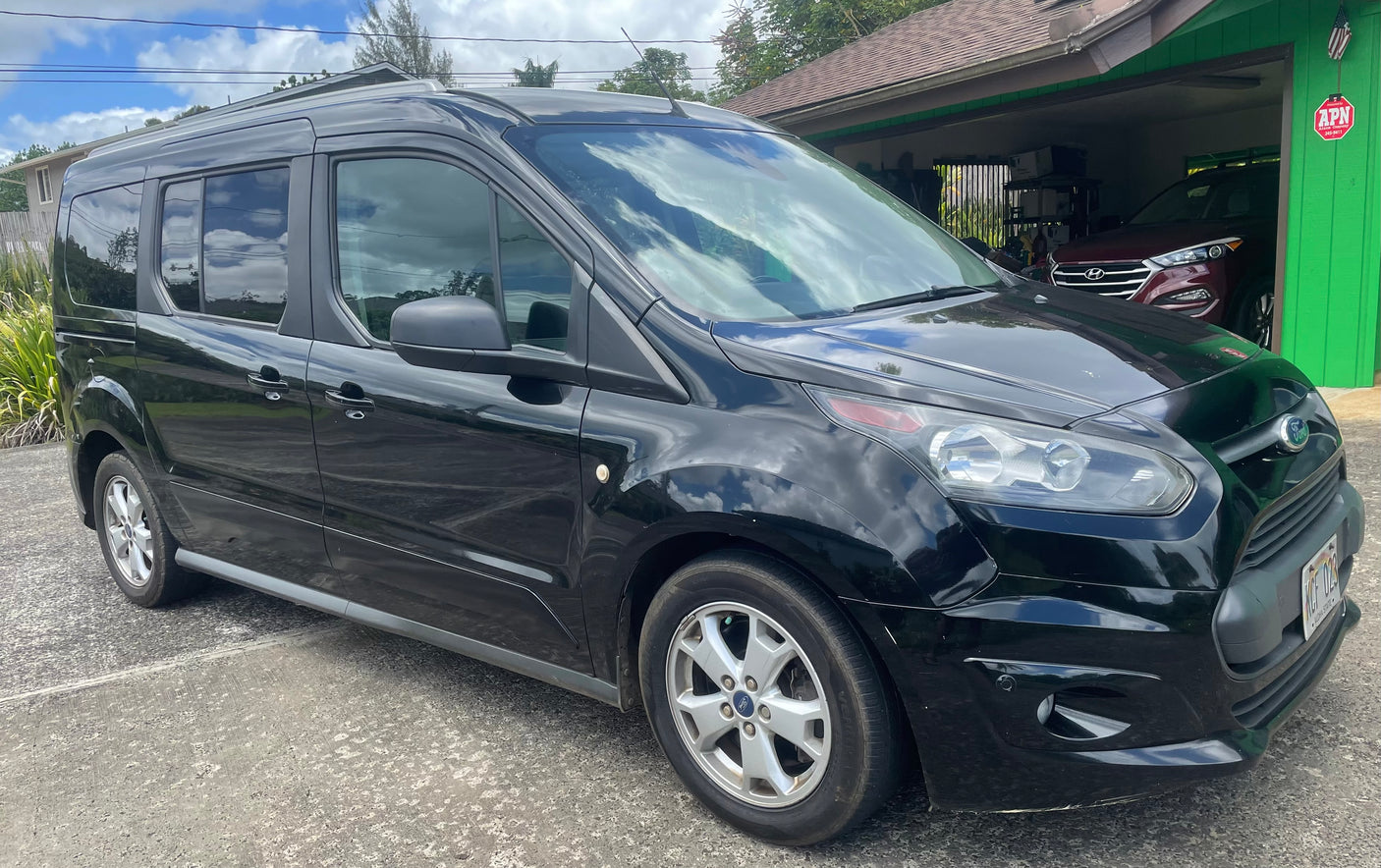 Black Ford Transit Connect van, ideal for RV rental adventures, parked on a driveway beside a home with a green garage.