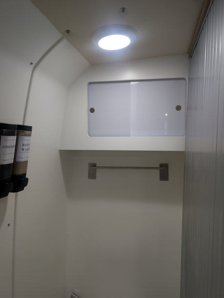 RV rental shower: compact white interior with mounted CONDITION and BODY WASH dispensers, overhead light, and towel bar.