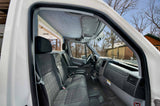 Experience this cozy rv rental's front cab, featuring dark gray seats, a functional dashboard, and a clear view of the winter scenery.