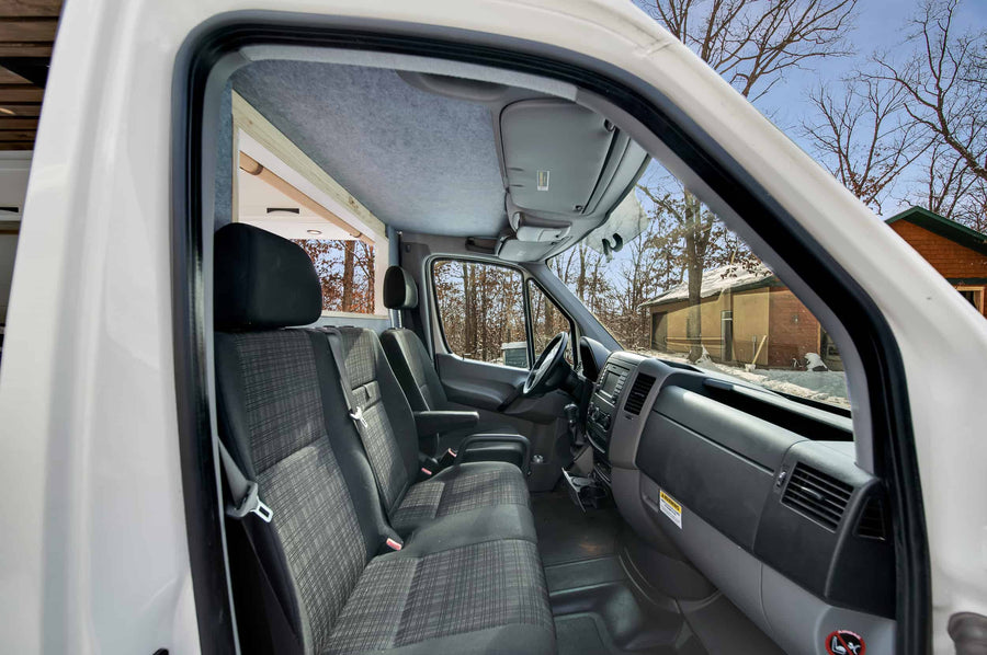 Experience this cozy rv rental's front cab, featuring dark gray seats, a functional dashboard, and a clear view of the winter scenery.