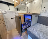 Modern RV rental interior: kitchenette, blue-lit fridge, bed, & cozy seating.