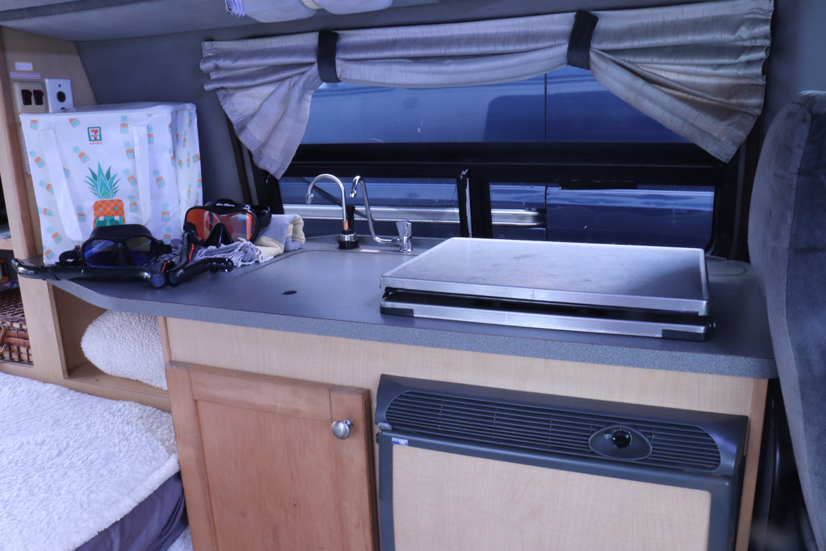 Inside an RV rental: a compact kitchen with sink, counter, fridge, and snorkel gear, ready for vacation travel. — photo 18