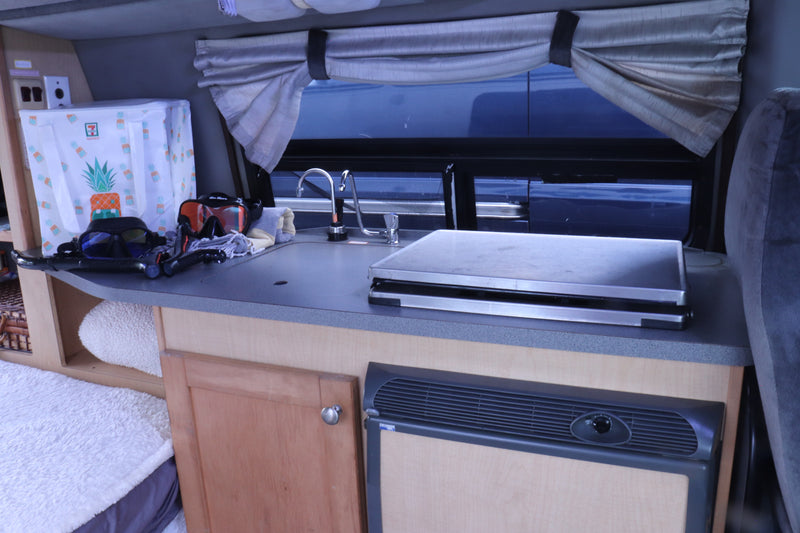 Inside an RV rental: a compact kitchen with sink, counter, fridge, and snorkel gear, ready for vacation travel. — photo 18