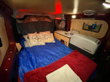 Cozy RV rental interior featuring a bed with pillows, compact kitchen with a sink, and Dometic cooler. Ideal for travel.