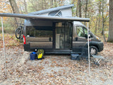 Dark grey camper van with pop-top roof and extended awning, perfect for an rv rental outdoor adventure. Bike, cooler, and camping gear seen.