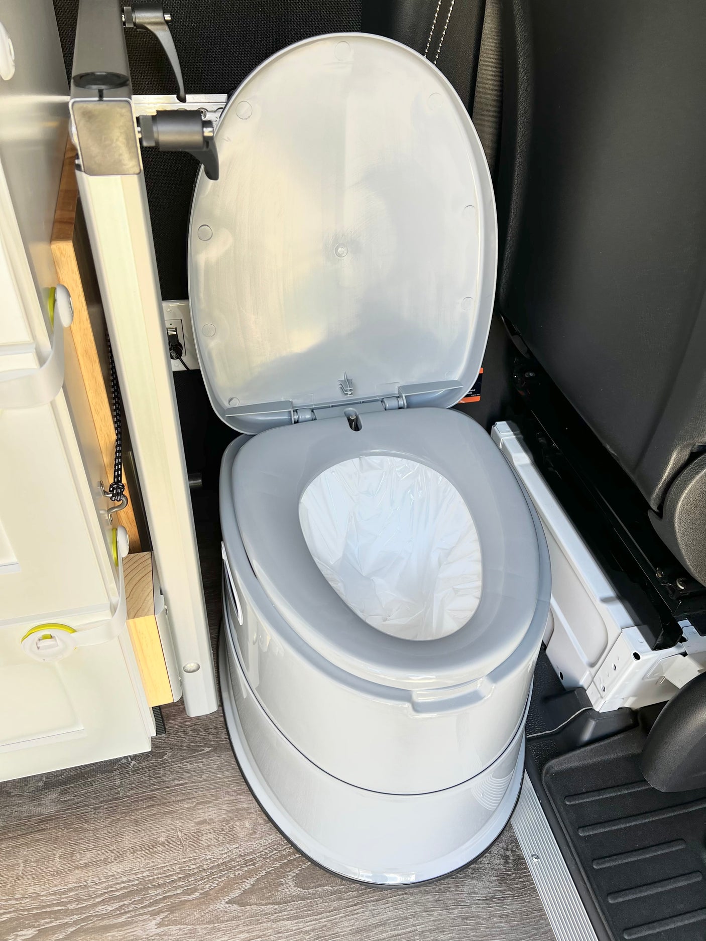 A clean, white portable toilet with an open lid and plastic liner, ready for use in an RV rental interior.