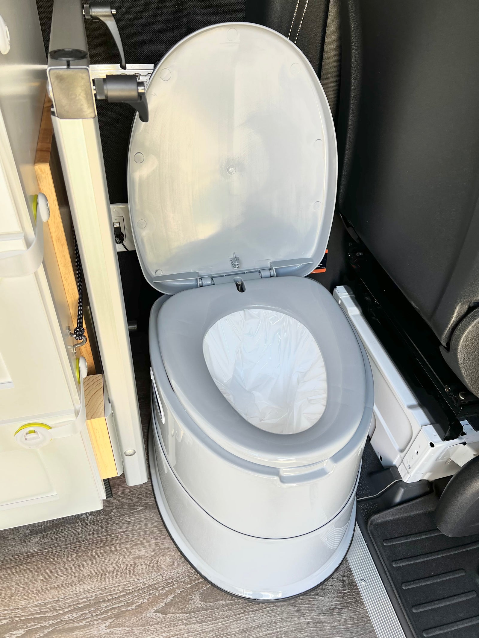 A clean, white portable toilet with an open lid and plastic liner, ready for use in an RV rental interior.