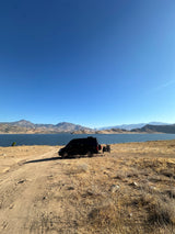 RV rental parked by a serene lake with scenic mountains and bikes, ready for an outdoor adventure.