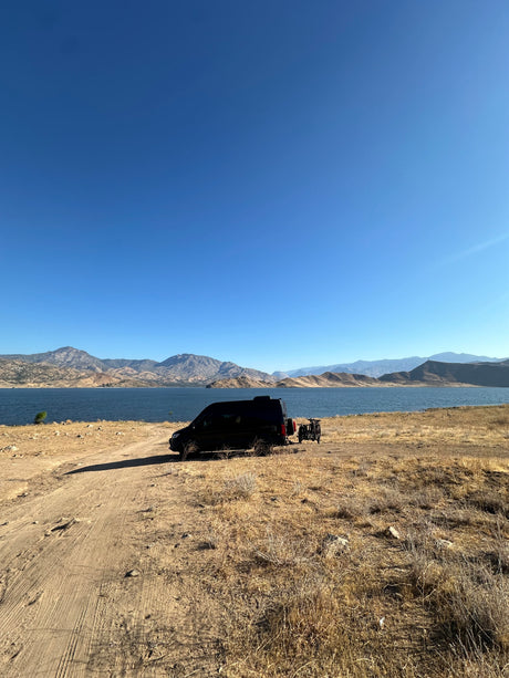 RV rental parked by a serene lake with scenic mountains and bikes, ready for an outdoor adventure.