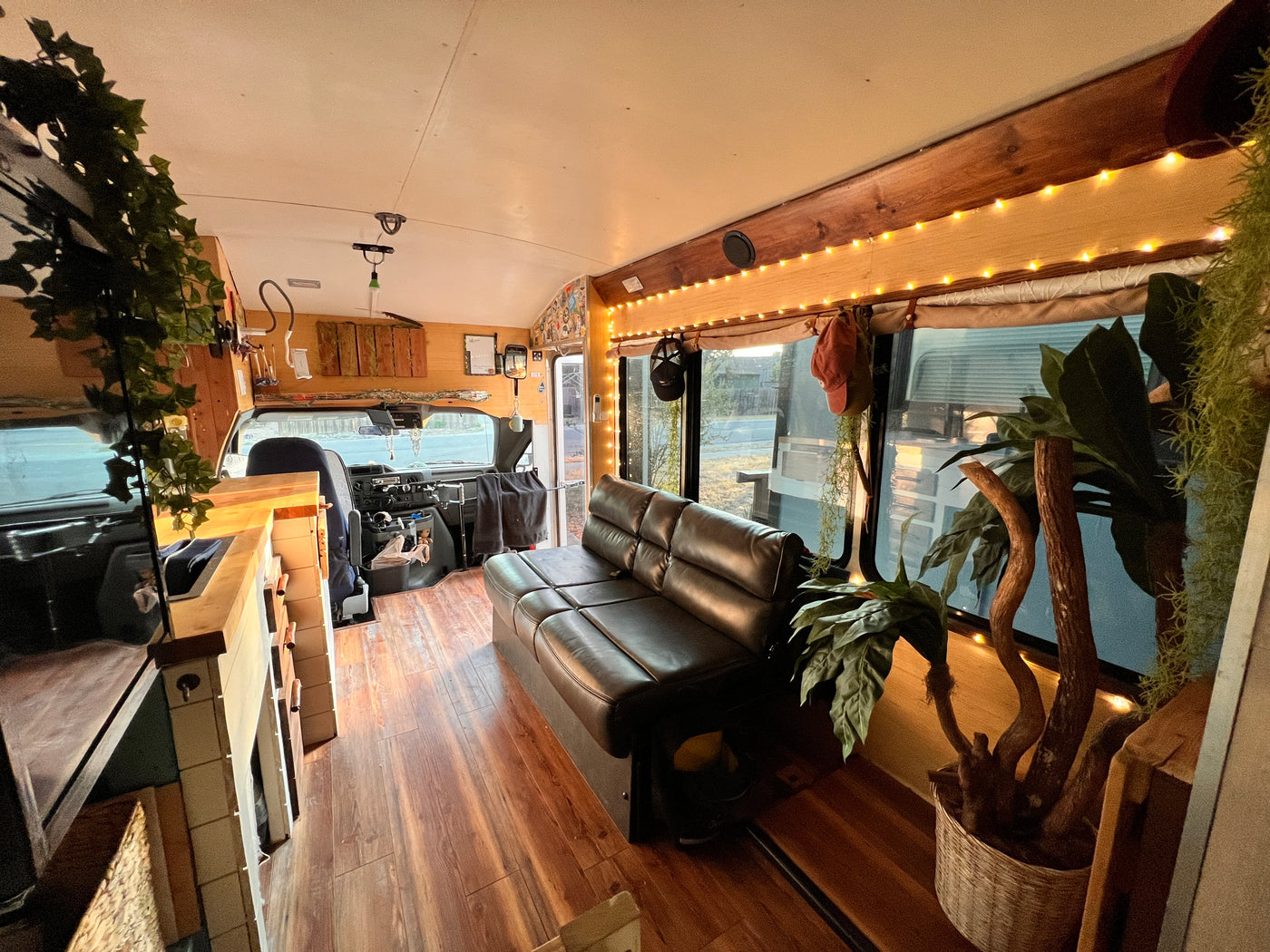 Inviting interior of a renovated bus, offering a cozy living space for an rv rental. Features sofa, wood floors, string lights, & plants. — photo 14