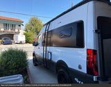 White Mercedes Sprinter rv rental camper van, customized with black accents, ladder, and off-road tires, parked outdoors.