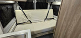 An rv rental's cream bench seat with two seatbelts. Features quilted design, sink, and window storage.