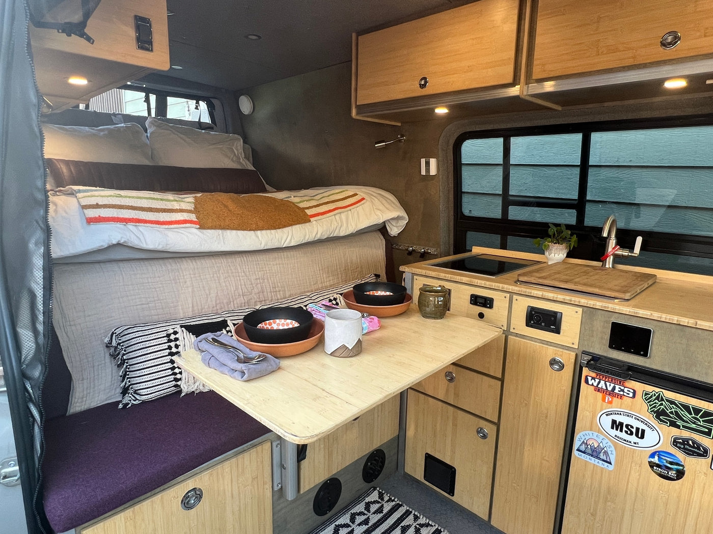 Well-designed RV rental interior featuring a comfortable bed, compact kitchen, and pull-out dining table. — photo 17