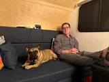 Man and his French bulldog relax on a dark blue couch inside a cozy rv rental.