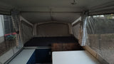 Inside an RV rental: a large bed, dining table, and plaid curtains define this pop-up camper's inviting interior.