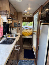 RV rental interior showcases a compact kitchen (sink, stove, fridge), adjacent shower, and a cozy bedroom at the rear.