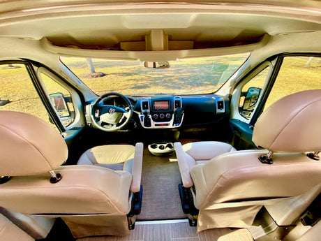 Inside an RV rental: view of the clean, tan-seated driver's cabin, dashboard, and steering wheel, ready for travel.