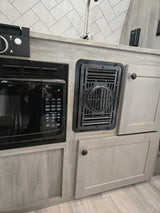 Compact rv rental kitchen featuring a microwave, cabinets, and essential vent, designed for efficiency and modern comfort.