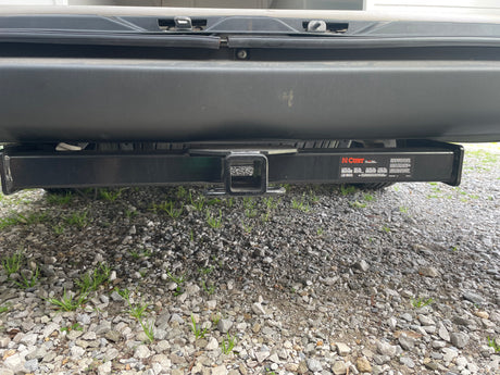 Back of an RV rental showing a black Curt trailer hitch receiver for towing. Gravel driveway below.