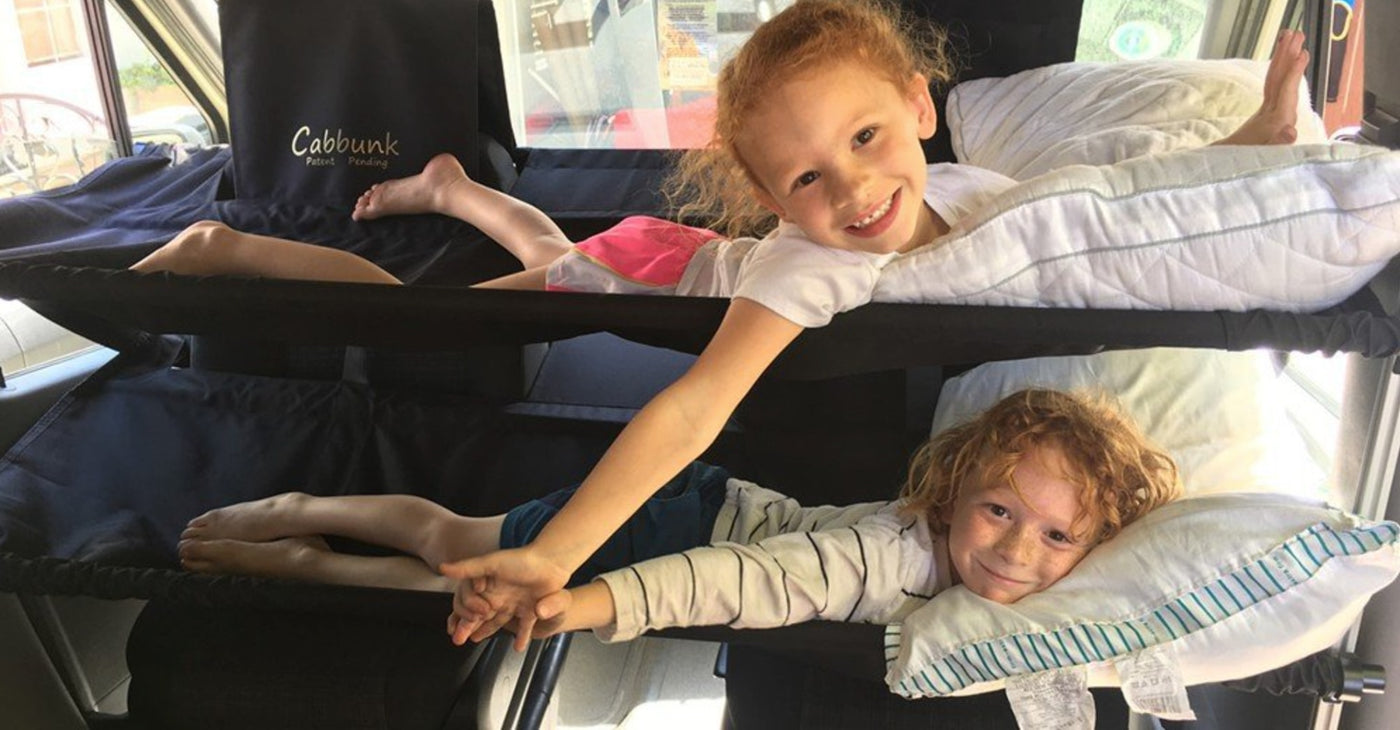 Two smiling kids hold hands from custom Cabbunk bunk beds, showing comfy family travel in an RV rental. — photo 13