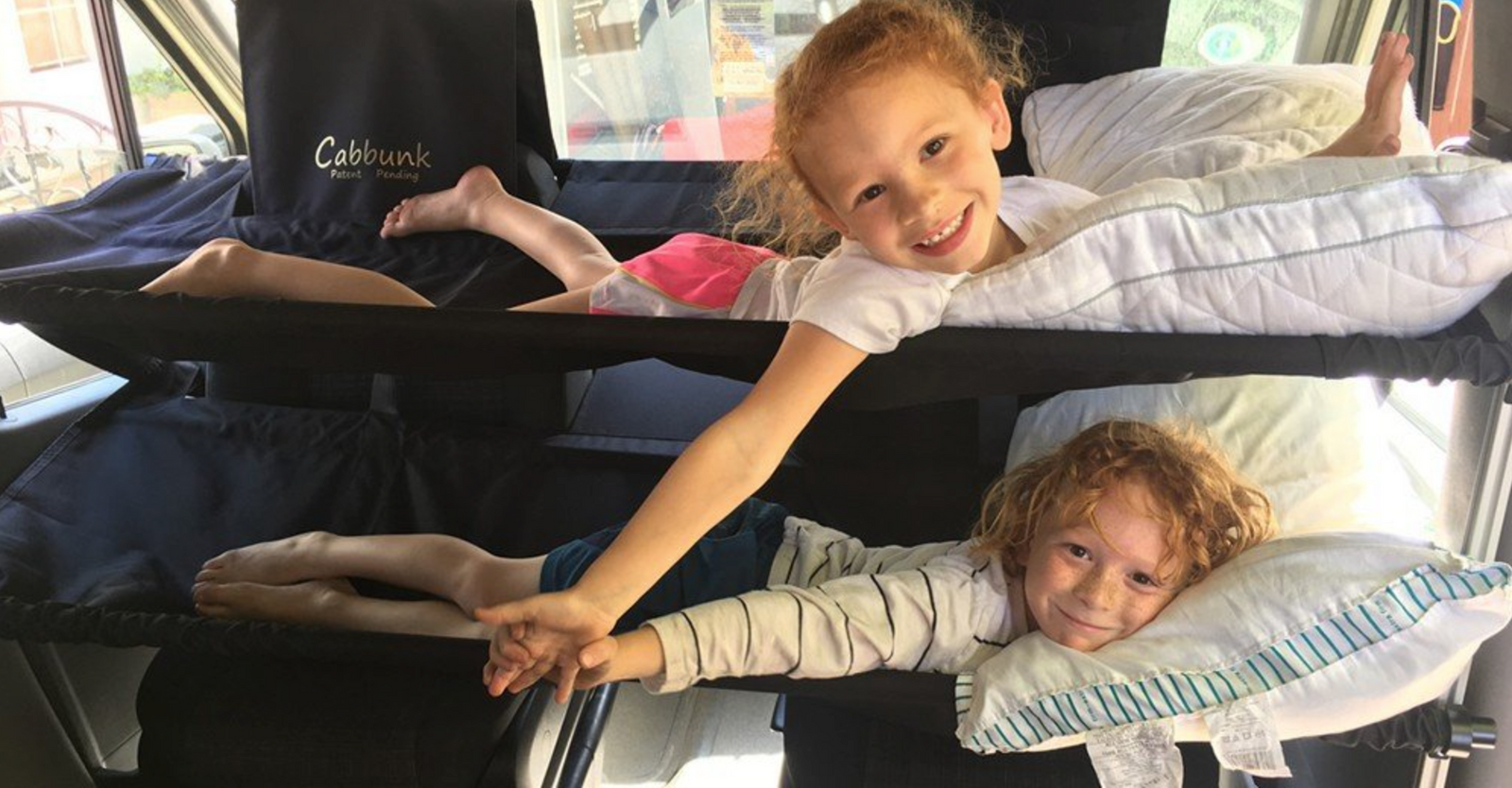 Two smiling kids hold hands from custom Cabbunk bunk beds, showing comfy family travel in an RV rental.