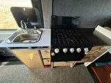 This RV rental kitchen features a modern stainless steel sink, a multi-burner gas stovetop, and practical storage drawers.