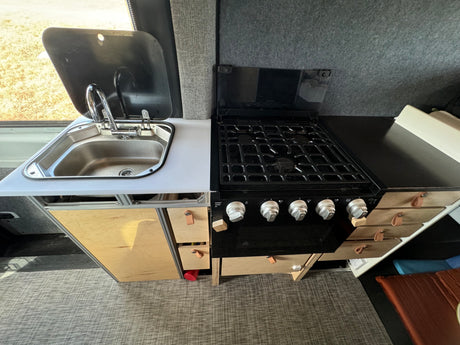 This RV rental kitchen features a modern stainless steel sink, a multi-burner gas stovetop, and practical storage drawers.